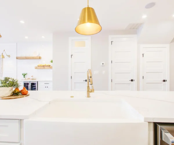 White quartz countertop, farmhouse sink and brass pendant, kitchen remodel by VKB Kitchen & Bath